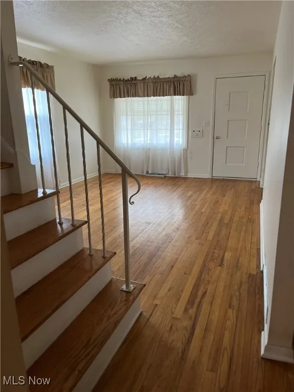 Stairway with wood finished floors and a textured ceiling
