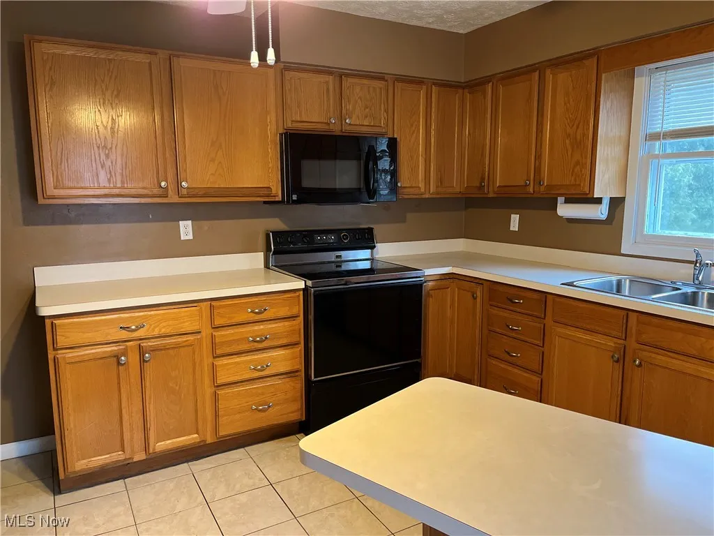 Kitchen featuring black appliances, light countertops, brown cabinetry, light tile patterned floors, and a textured ceiling