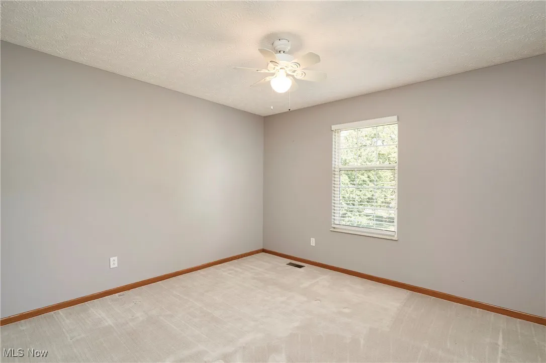 Empty room featuring a textured ceiling, light colored carpet, and a ceiling fan