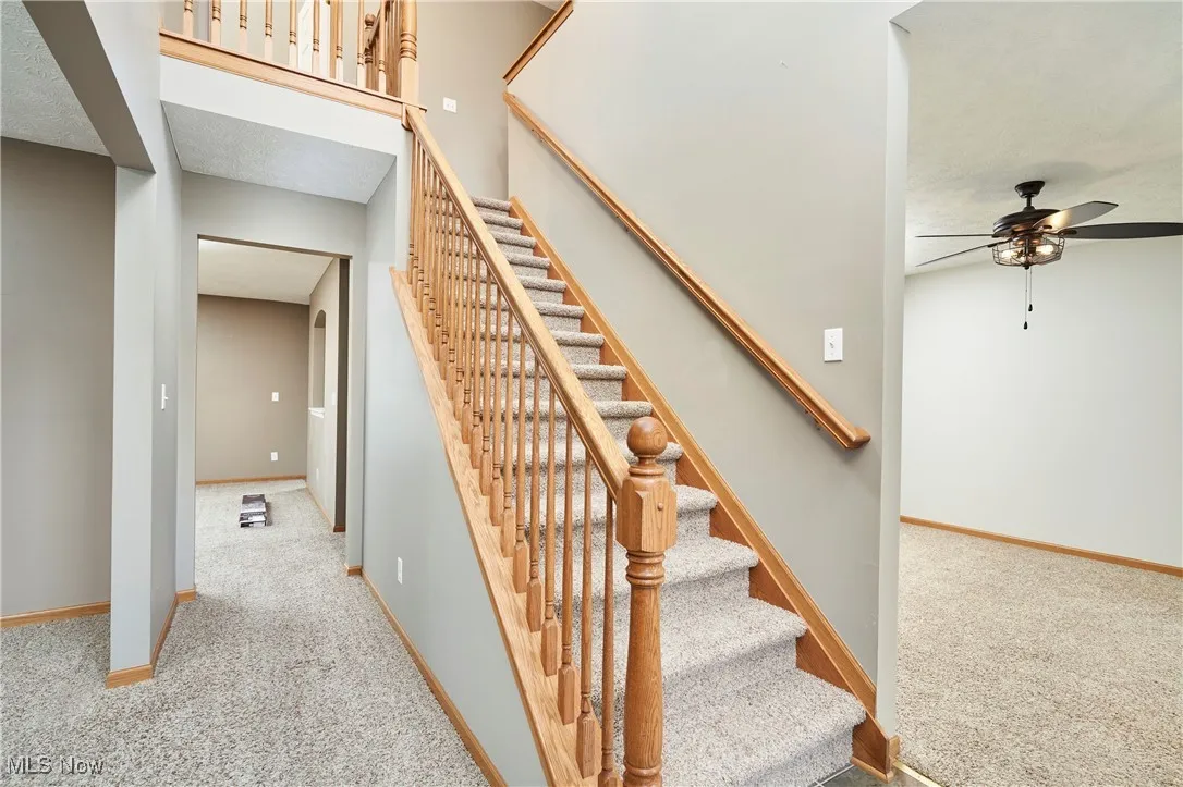 Staircase featuring carpet floors, ceiling fan, and a textured ceiling