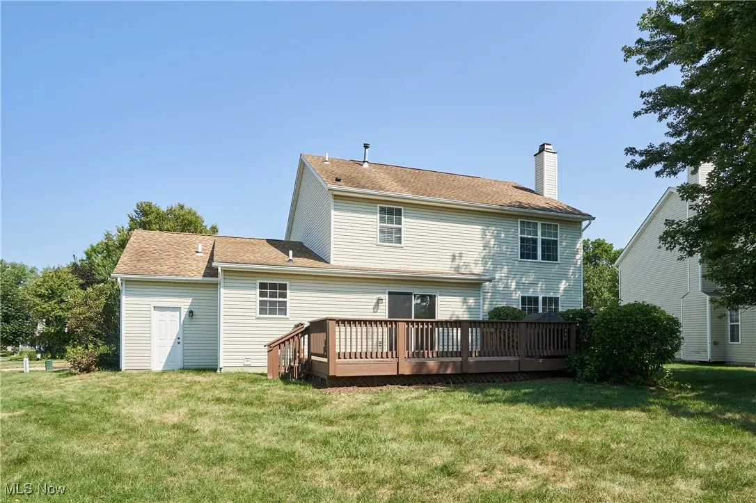 Rear view of property featuring a wooden deck, a chimney, a yard, and a shingled roof