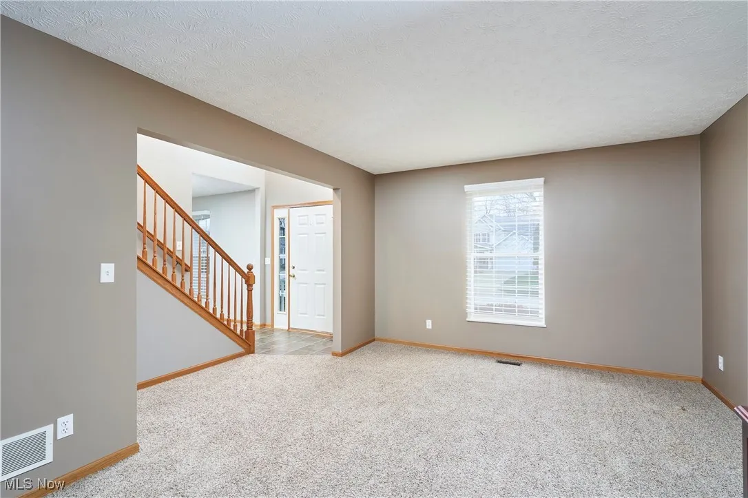 Carpeted empty room featuring a textured ceiling and stairway