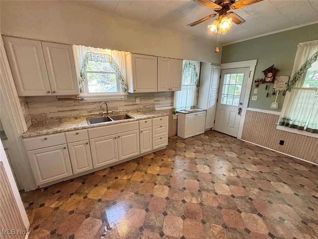 Kitchen featuring plenty of natural light, white cabinetry, wainscoting, crown molding, and ceiling fan