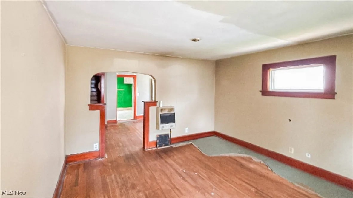 Unfurnished room featuring arched walkways, wood finished floors, and heating unit