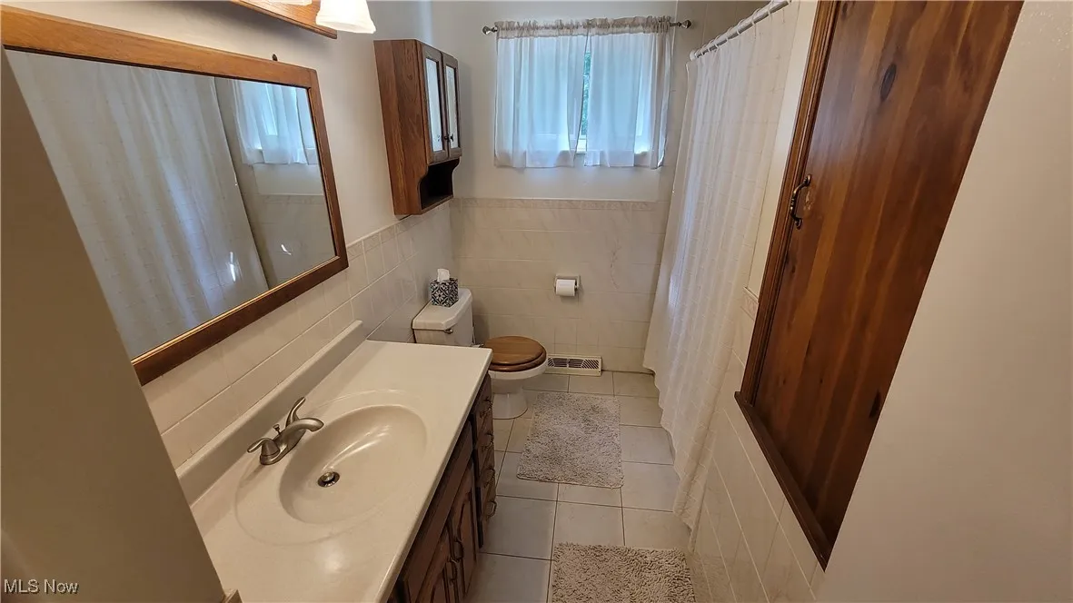 Bathroom with tile walls, light tile patterned flooring, vanity, a wainscoted wall, and curtained shower