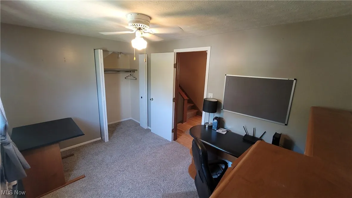 Bedroom currently used as office area featuring light colored carpet and a ceiling fan