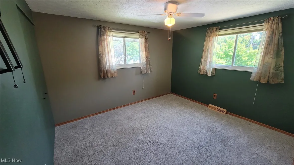 Carpeted empty room with ceiling fan and a textured ceiling