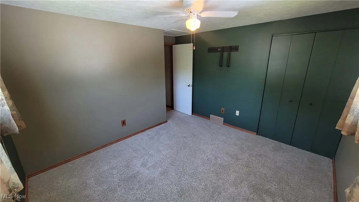 Unfurnished bedroom with a textured ceiling, carpet flooring, ceiling fan, and a closet