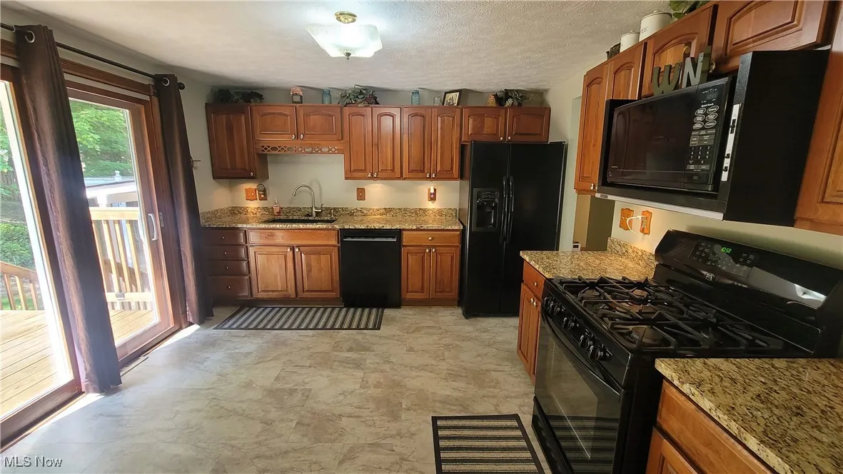 Kitchen featuring black appliances, light stone counters, brown cabinetry, and a textured ceiling