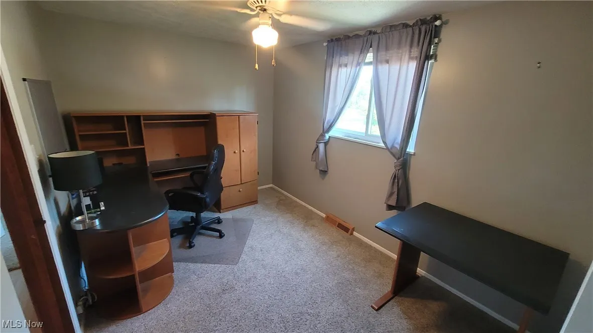 Bedroom currently used as office area featuring light colored carpet and a ceiling fan
