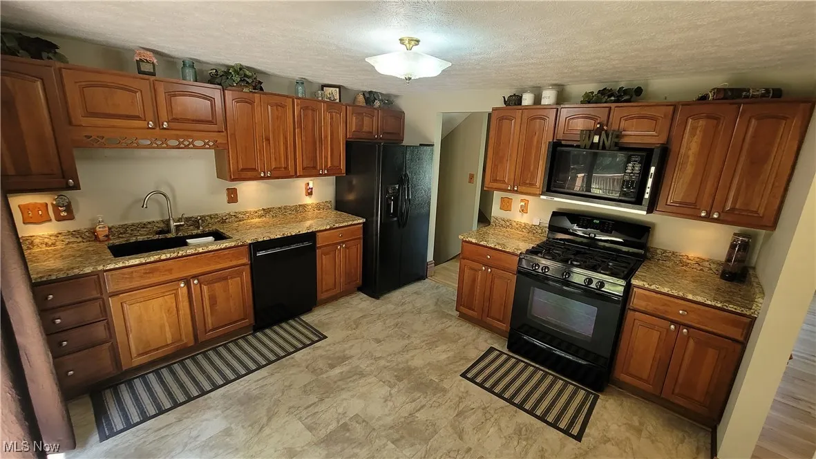 Kitchen featuring black appliances, brown cabinets, a textured ceiling, and light stone countertops