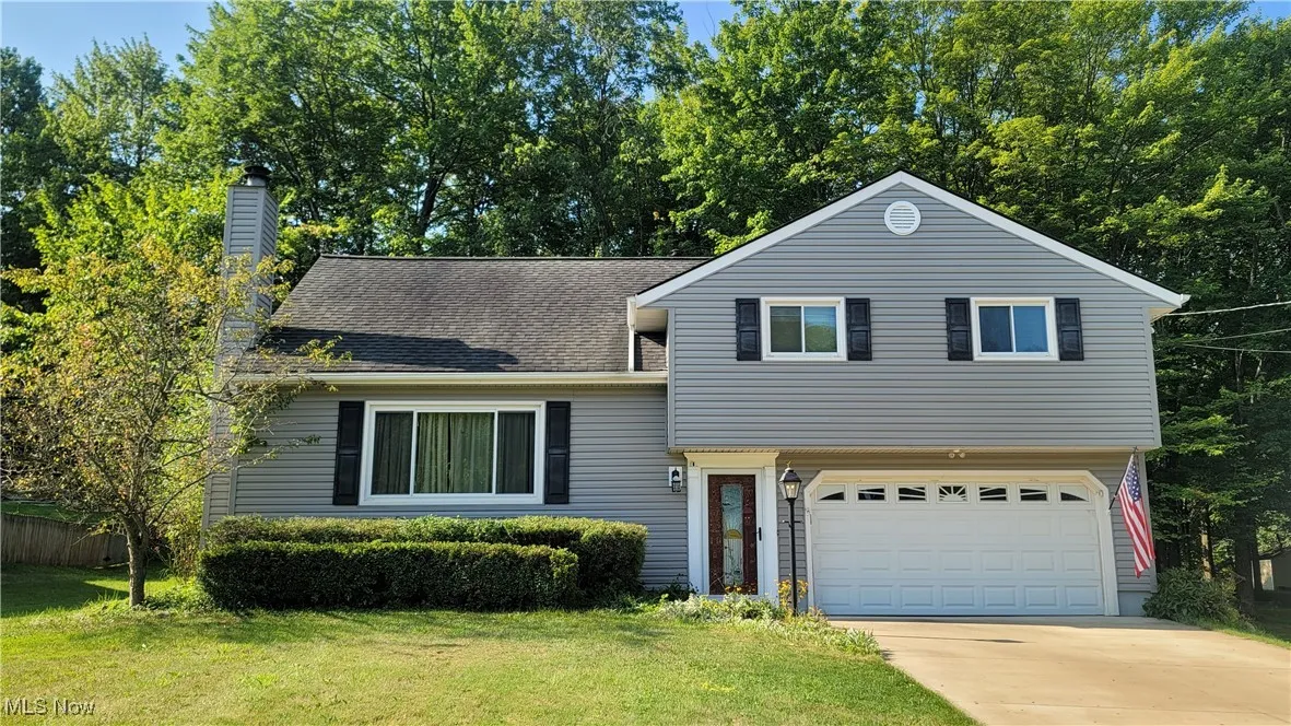 Split level home with driveway, an attached garage, a chimney, a front lawn, and roof with shingles