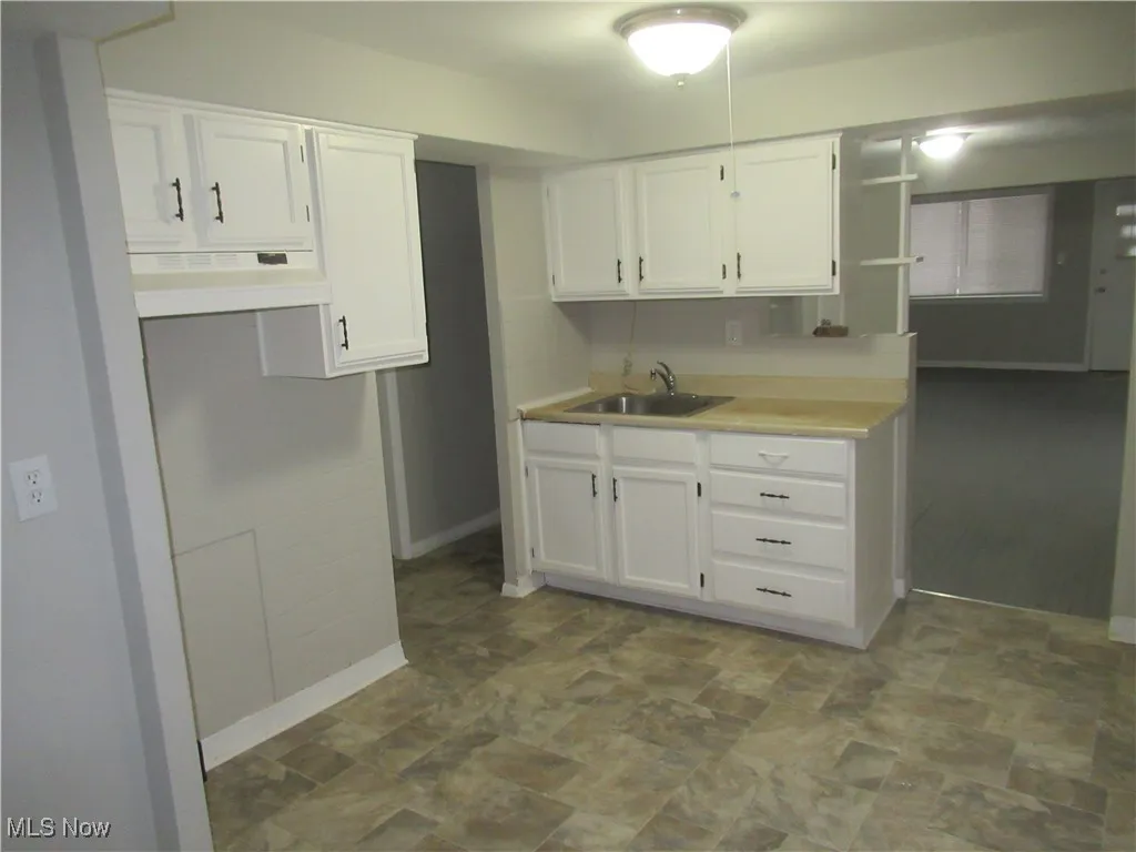 Kitchen with light countertops, white cabinetry, under cabinet range hood, and stone finish flooring