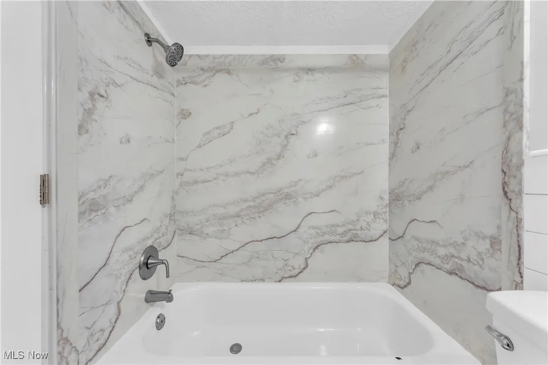 Bathroom with a textured ceiling and  shower combination