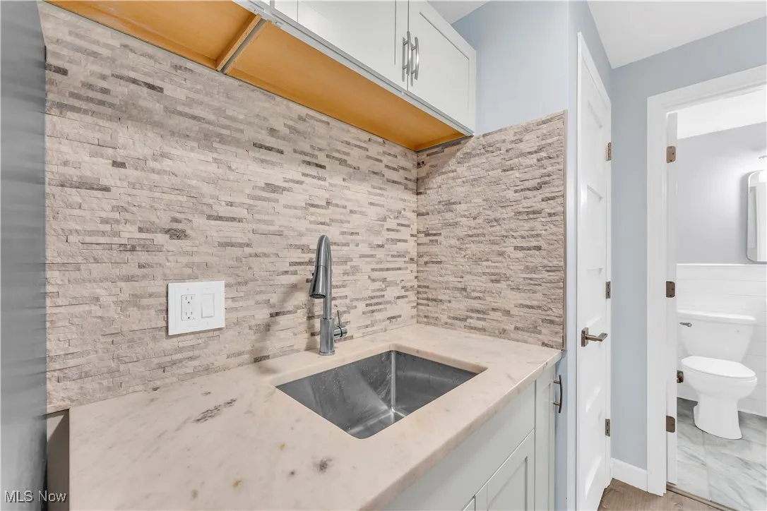 Kitchen featuring white cabinets, light stone countertops, and decorative backsplash