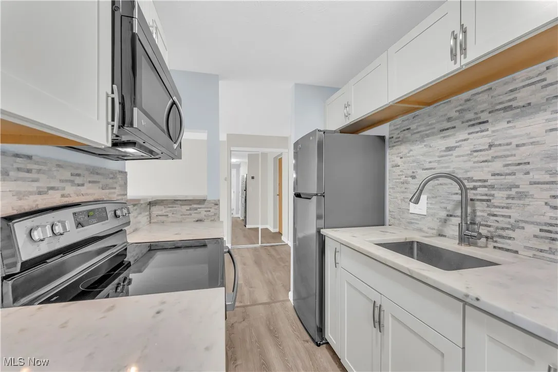 Kitchen with decorative backsplash, white cabinets, and stainless steel appliances