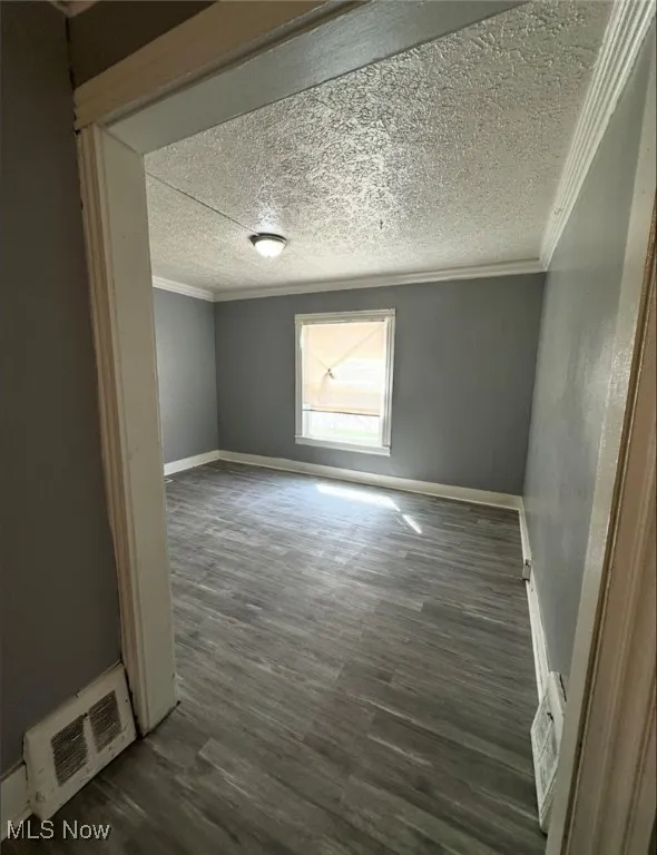 Unfurnished room featuring dark wood finished floors, ornamental molding, and a textured ceiling