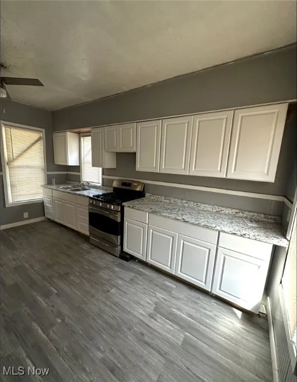 Kitchen featuring white cabinetry, stainless steel gas stove, light stone counters, dark wood-style flooring, and a ceiling fan