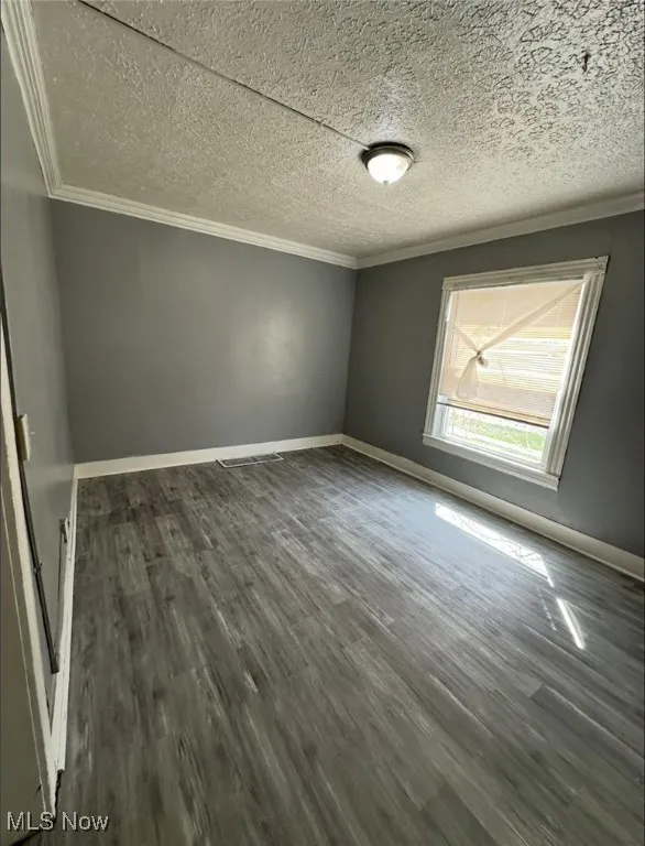 Empty room featuring ornamental molding, dark wood-style flooring, and a textured ceiling