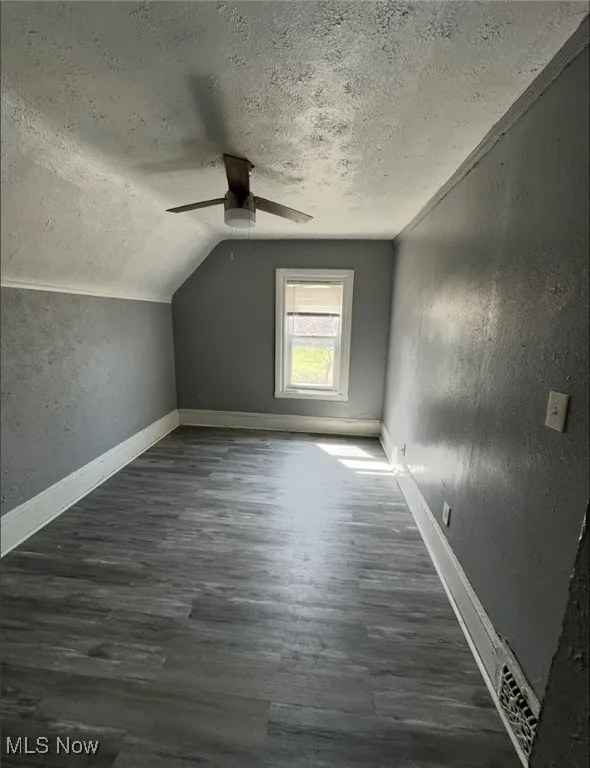 Bonus room featuring a textured wall, dark wood-style flooring, a textured ceiling, vaulted ceiling, and a ceiling fan