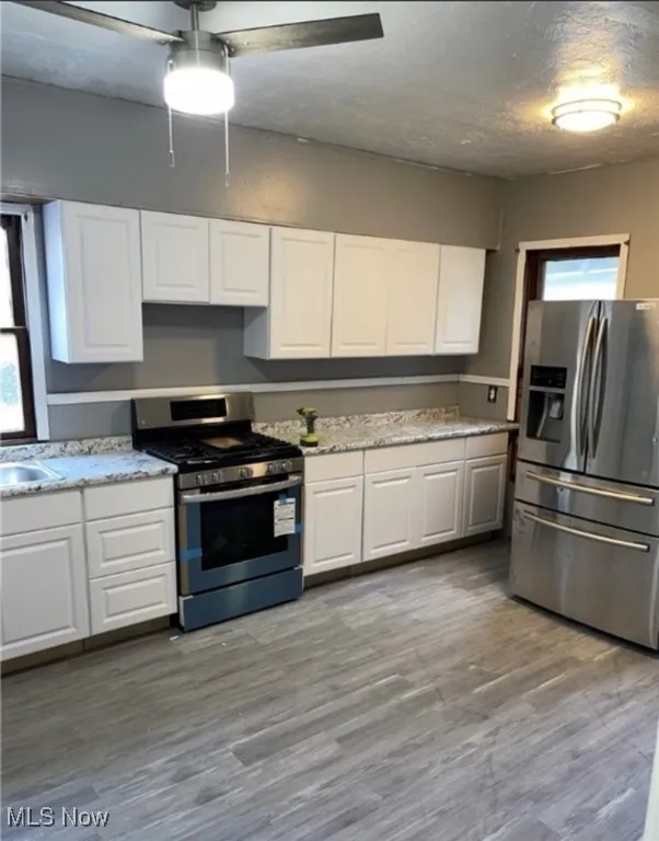 Kitchen with stainless steel appliances, white cabinets, dark wood-style flooring, light stone countertops, and a textured ceiling