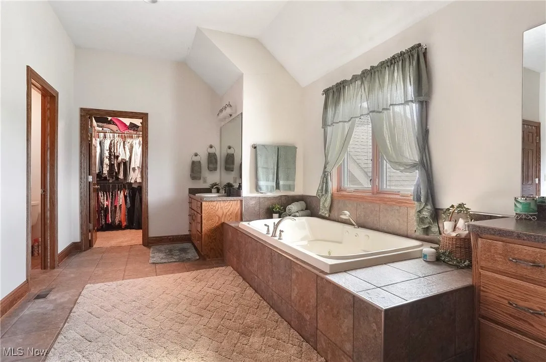 Bathroom featuring vanity, a whirlpool tub, lofted ceiling, a spacious closet, and light tile patterned floors