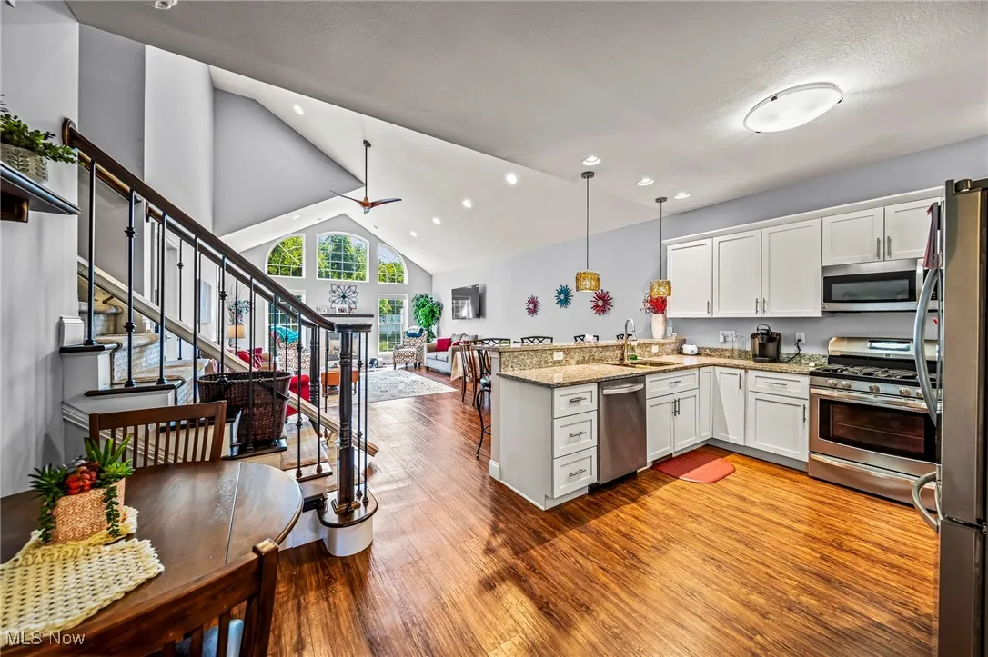 Kitchen featuring white cabinets, a peninsula, stainless steel appliances, hanging light fixtures, and high vaulted ceiling