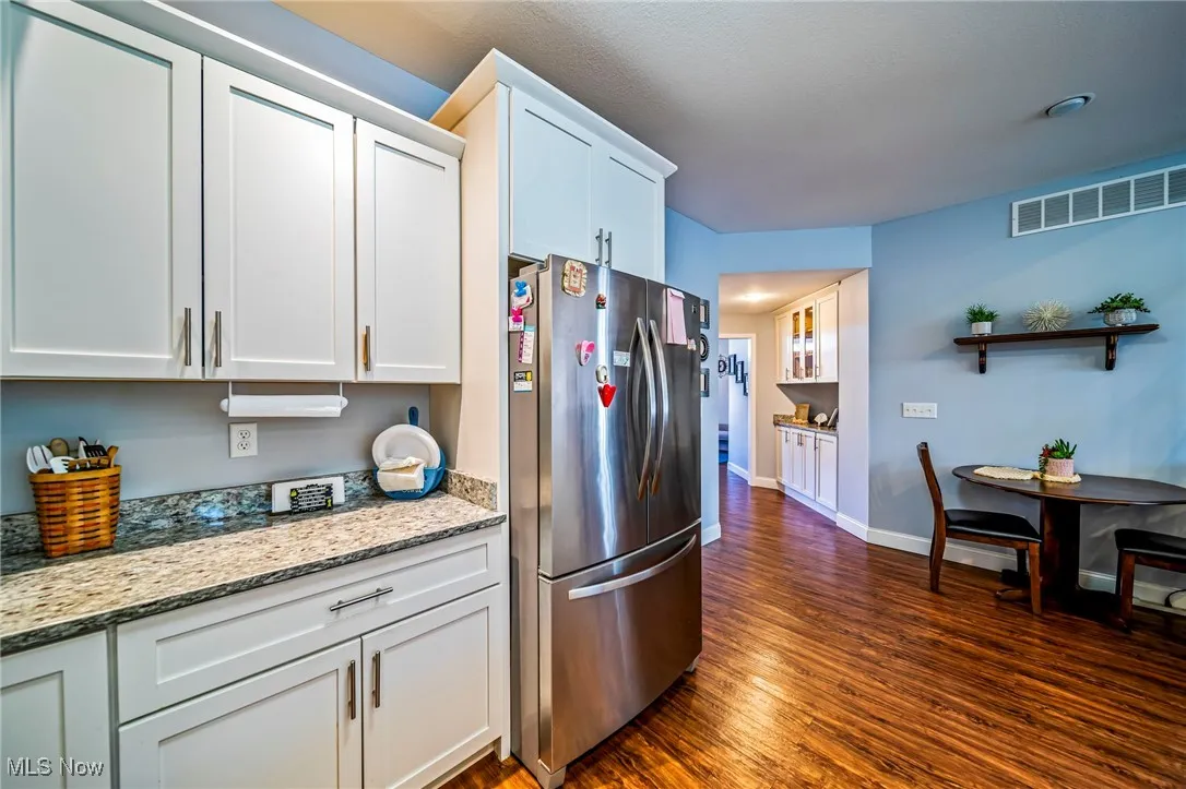 Kitchen featuring freestanding refrigerator, white cabinetry, light stone counters, and dark wood-style floors