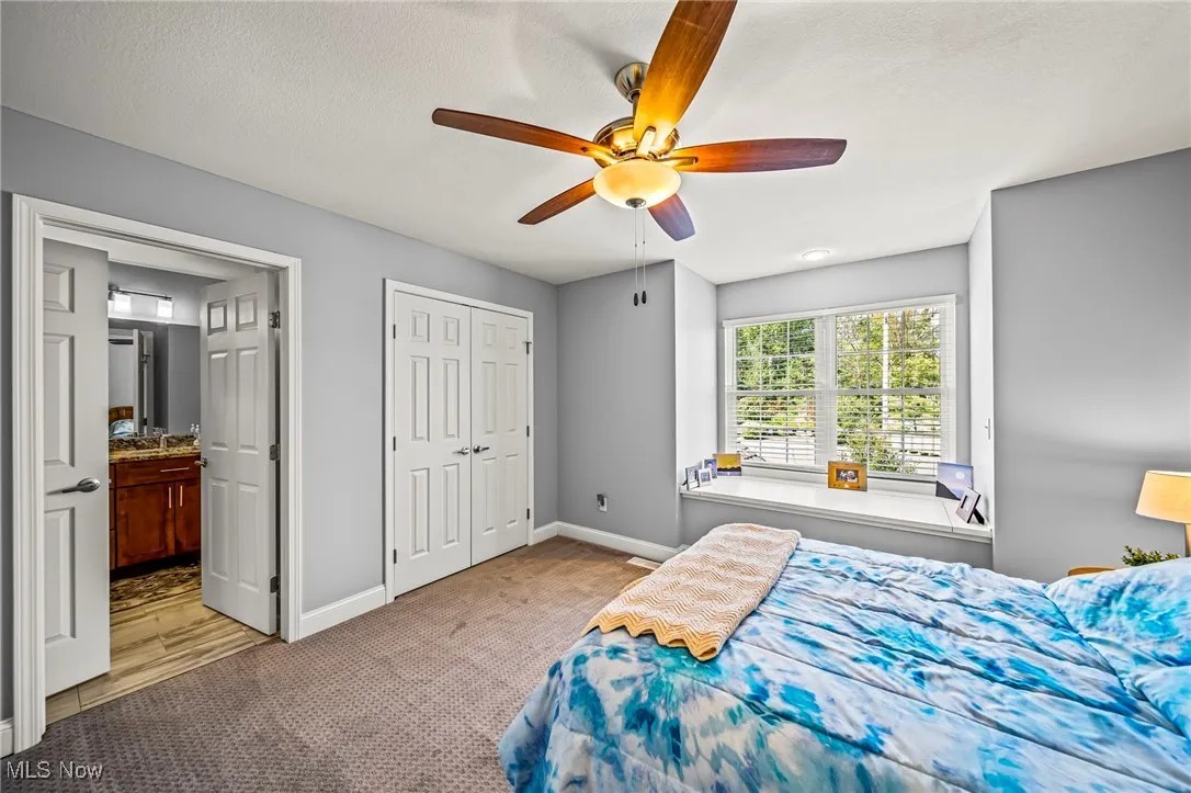 Bedroom with light carpet, ceiling fan, a textured ceiling, connected bathroom, and a closet
