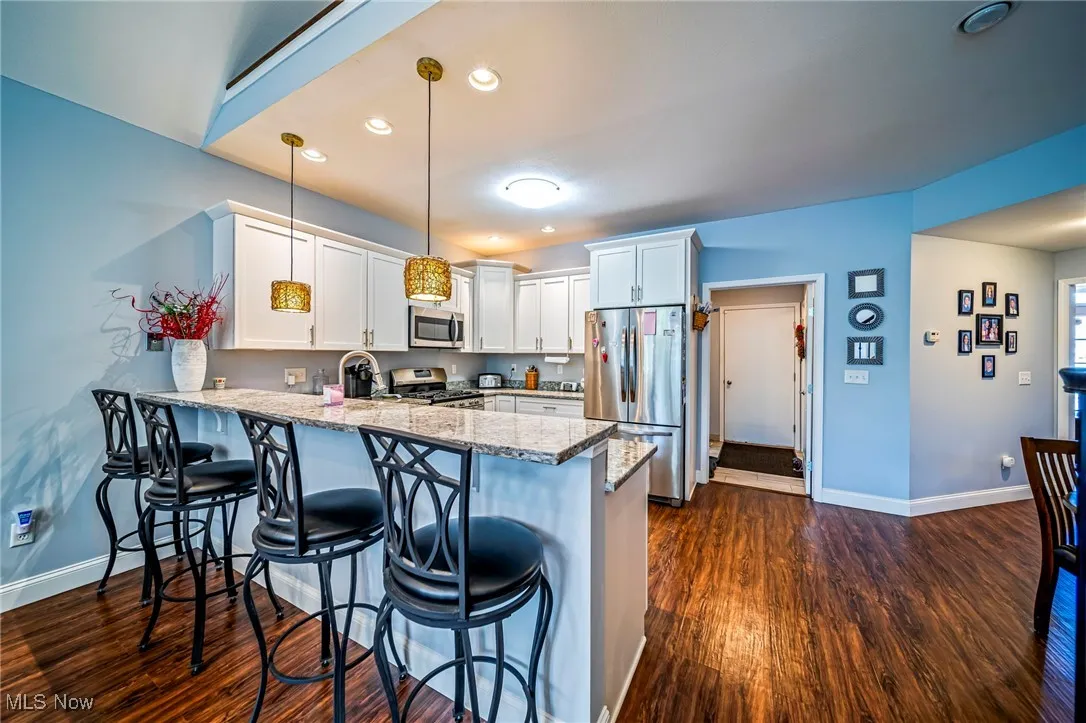 Kitchen featuring a peninsula, white cabinets, light stone countertops, stainless steel appliances, and a kitchen breakfast bar