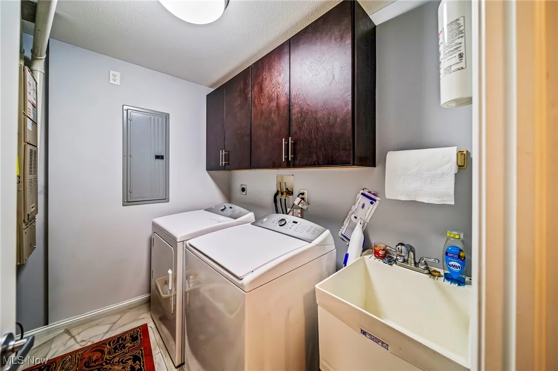 Laundry area featuring cabinet space, washing machine and clothes dryer, electric panel, and a textured ceiling