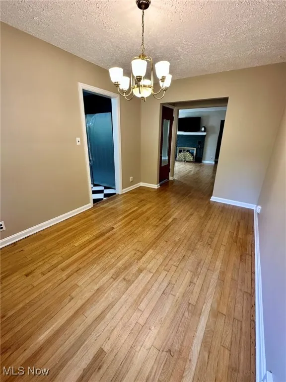 Unfurnished dining area with a chandelier, light wood finished floors, a textured ceiling, and a fireplace