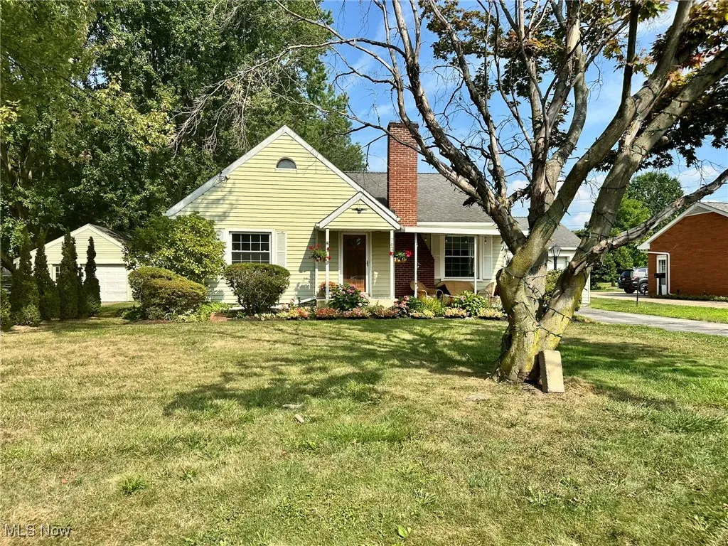 View of front of property featuring a garage, a front lawn, a chimney, and an outbuilding