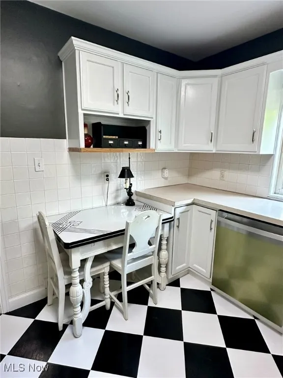Kitchen featuring light floors, white cabinets, light countertops, stainless steel dishwasher, and backsplash