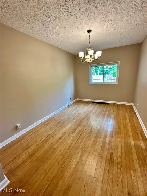 Empty room featuring hardwood / wood-style floors, a chandelier, and a textured ceiling