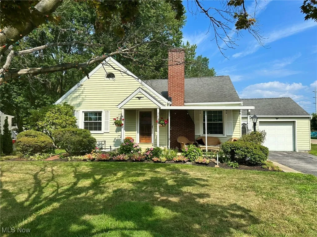 View of front facade with a garage, a chimney, a porch, a front yard, and a shingled roof
