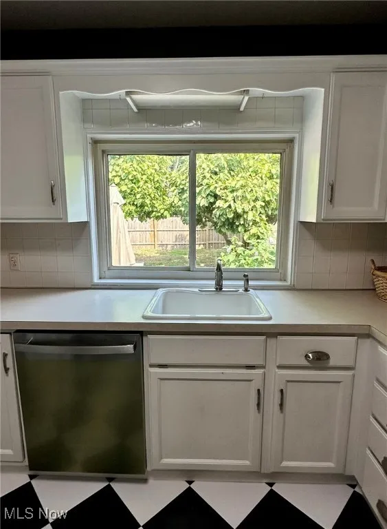 Kitchen featuring white cabinetry, decorative backsplash, light countertops, and dishwasher