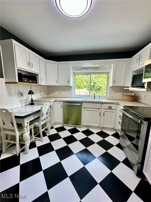Kitchen with dark flooring, backsplash, white cabinets, and appliances with stainless steel finishes