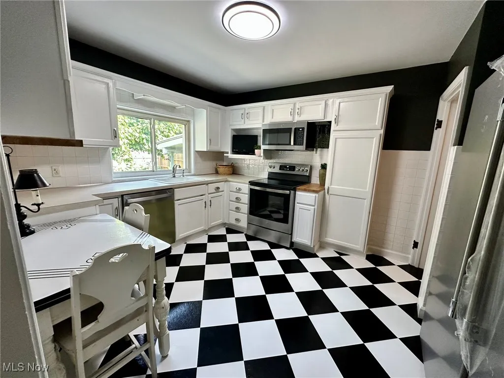 Kitchen with dark flooring, light countertops, white cabinetry, appliances with stainless steel finishes, and tile walls