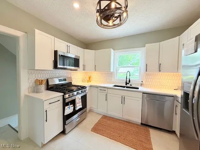 Kitchen featuring stainless steel appliances, a textured ceiling, white cabinets, and decorative backsplash