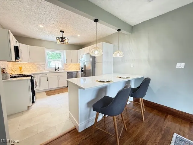 Kitchen with a breakfast bar, hanging light fixtures, backsplash, stainless steel appliances, and a peninsula