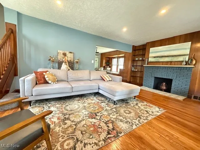 Living area with a textured ceiling, a brick fireplace, wood finished floors, stairway, and wood walls