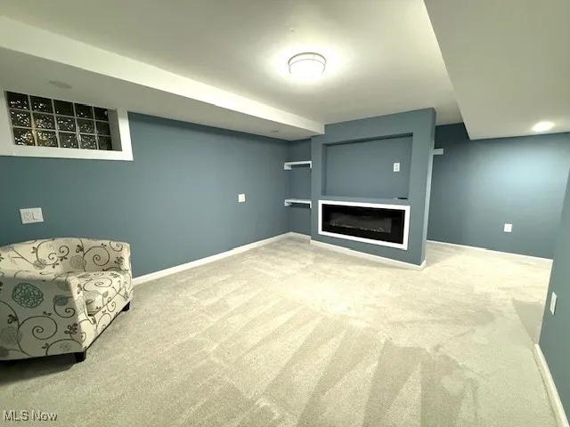 Unfurnished room featuring carpet and a glass covered fireplace