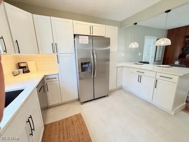 Kitchen with appliances with stainless steel finishes, a peninsula, hanging light fixtures, white cabinets, and a textured ceiling