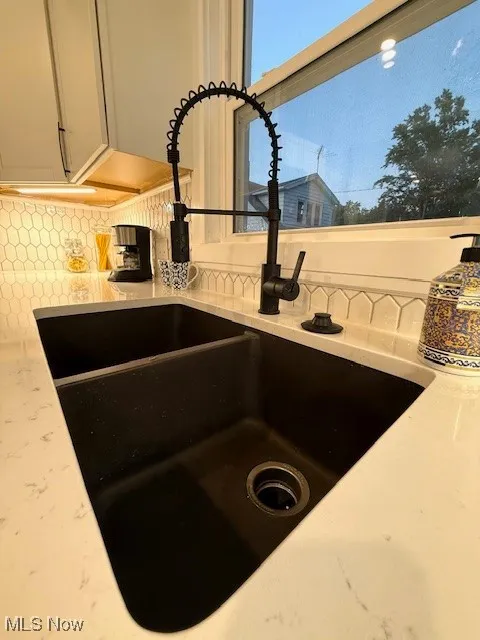 Kitchen view of decorative backsplash, light stone counters, and white cabinetry