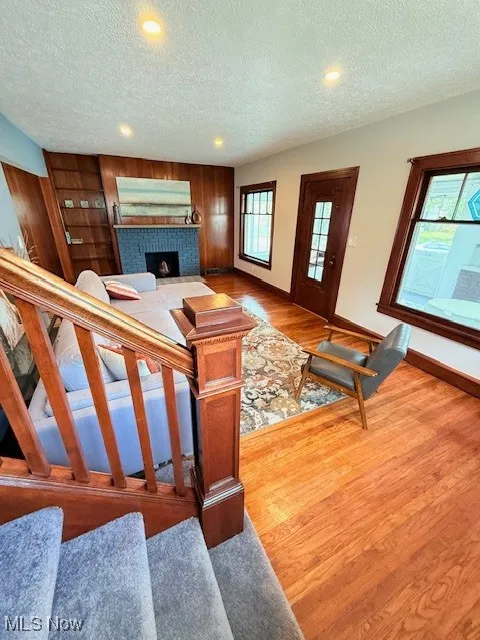 Living room with light wood-style flooring, a textured ceiling, a fireplace, wood walls, and recessed lighting