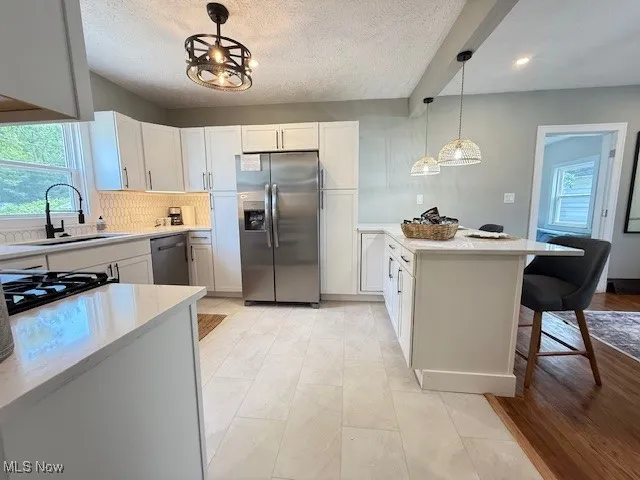 Kitchen with appliances with stainless steel finishes, white cabinets, decorative light fixtures, light stone counters, and tasteful backsplash