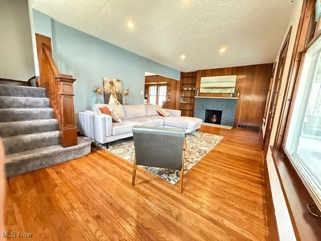 Living room with a textured ceiling, stairs, a fireplace, light wood-style flooring, and wooden​​‌​​​​‌​​‌‌​‌‌​​​‌‌​‌​‌​‌​​​‌​​ walls