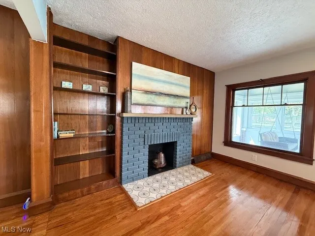Unfurnished living room with a brick fireplace, wooden walls, a textured ceiling, and light wood finished floors