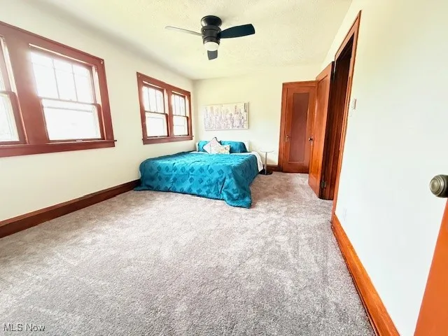 Bedroom with light carpet, ceiling fan, and a textured ceiling